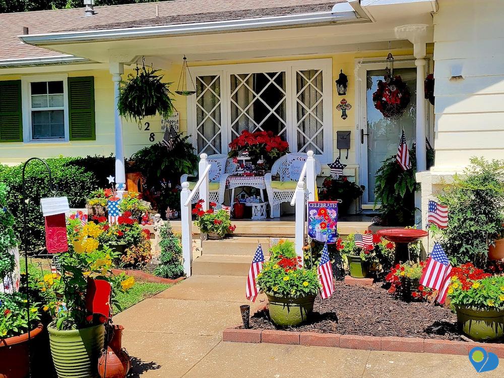 Sunny front yard and covered porch all decorated with colorful flowers and US flags for the Fourth of July holiday