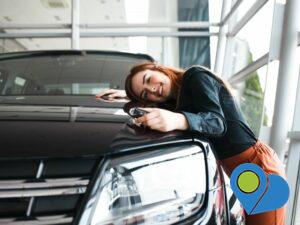 woman leaning her face on the hood of a new car holding the keys inside the dealership