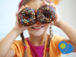 child holding chocolate-frosted donuts with multi-colored sprinkles over her eyes like glasses