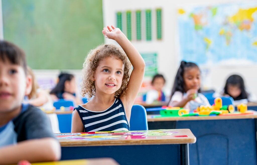 elementary age girl raising her hand in class