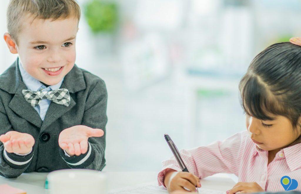 boy at a table holding up hands like he's weighing options and a girl writing on paper