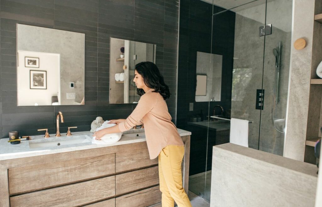 photo of a woman folding a towel on the counter of a modern-looking bathroom
