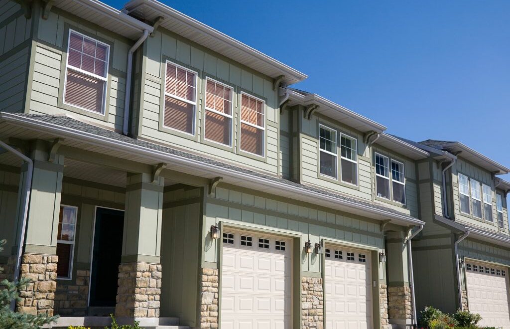 Close-up photo of subdued green craftsman-style, two-story townhomes with rock wainscoting