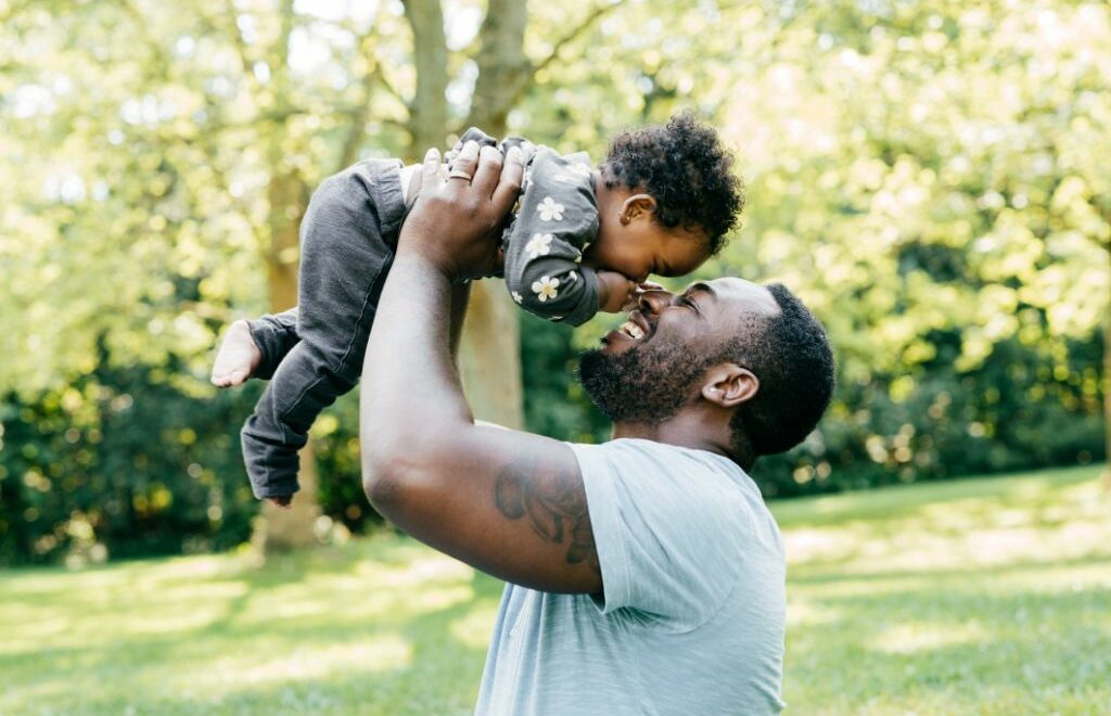 father holding baby above his head touching noses
