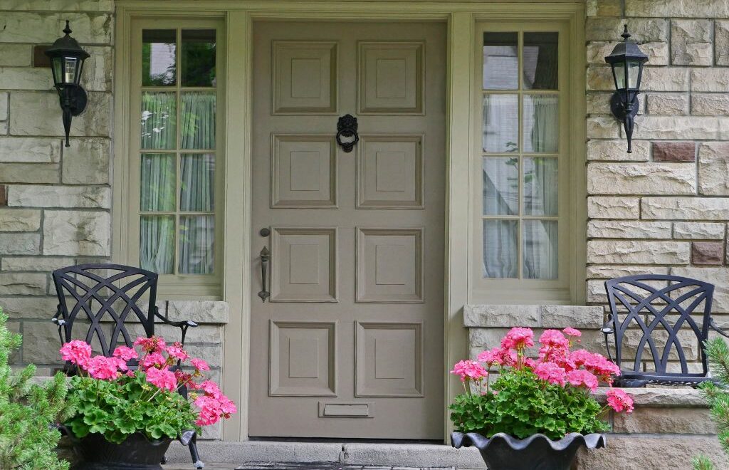 Front porch with neutral, monochromatic taupe color with two pots of pretty pink geraniums on each side of the front door
