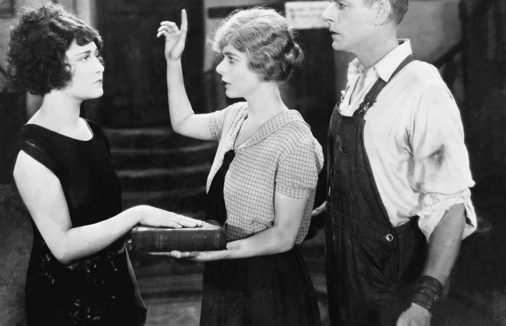 Vintage black and white photo of a woman holding up her hand while another woman has her right hand on a Bible and a man looking on