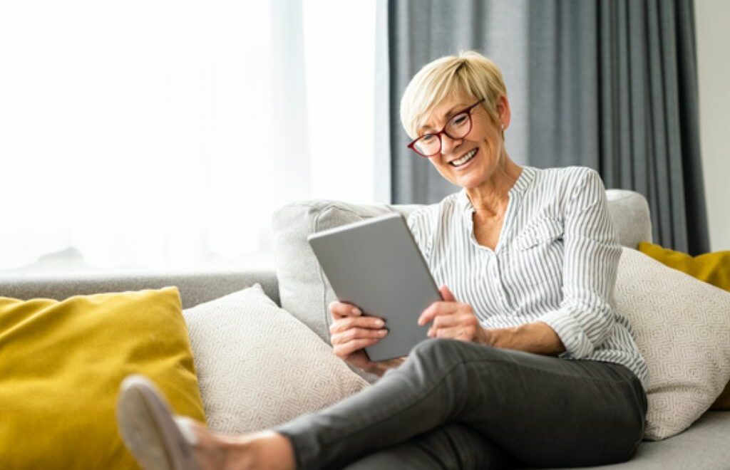 woman stretched out sofa smiling as she reads her tablet device
