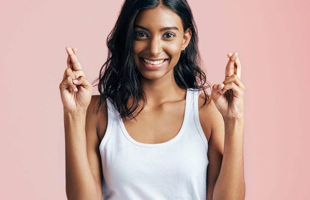A smiling young woman holding up both hands with her fingers crossed